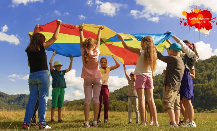 Kinder auf Wiese mit Regenbogentuch