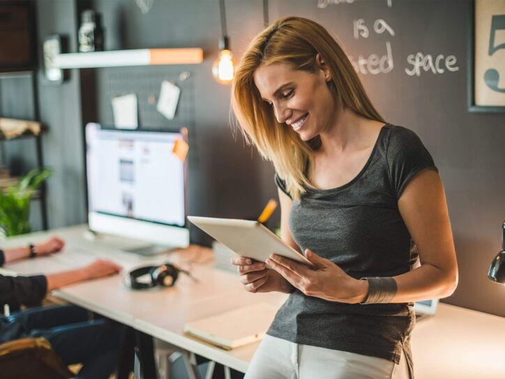 Eine lächelnde Frau steht im Büro mit einem Tablet in der Hand